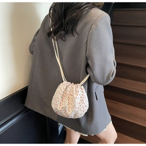 Close-up of white floral bucket bag with drawstring closure and slim shoulder strap