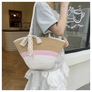 Detail of three-tone striped woven tote bag with white rope handles and a lace bow charm