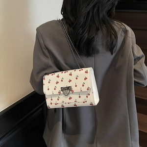 Sac bandoulière blanc à motif cerises et chaîne métallique porté par un mannequin