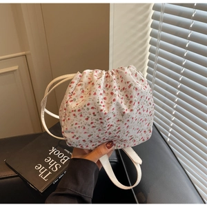 Detailed shot of white floral drawstring bucket bag with pink flower patterns and leather strap