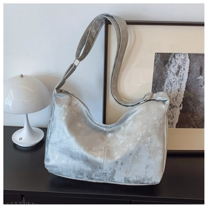 Metallic silver hobo bag with worn texture and buckle detail on black wooden table