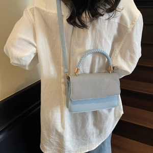Light blue crossbody bag with woven texture flap and adjustable strap shown on model