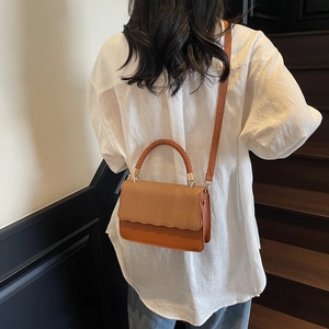 Minimalist orange-brown woven flap crossbody bag shown on model in a modern interior