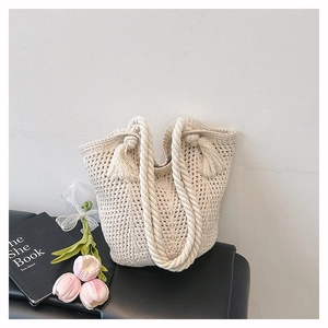 Detail of bohemian cream woven tote bag with fringe tassels and rope handles on black seat