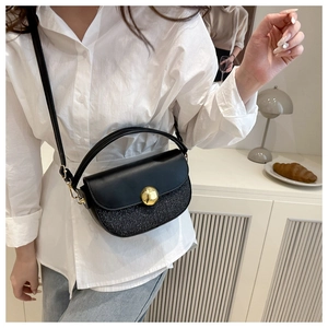 Detail of black patchwork saddle bag with gold metal clasp and adjustable leather strap