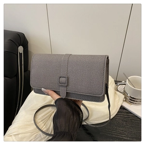 Detailed view of gray textured crossbody bag with square buckle held in a casual setting