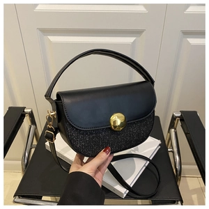 Detail of black saddle bag with sequin panel and gold metal buckle on a black chair