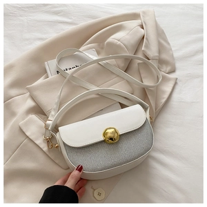 Detail of minimalist saddle bag featuring cream leather flap and gold metal buckle