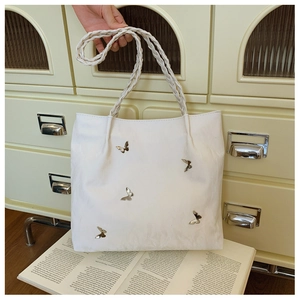 Dettaglio borsa tote in pelle bianca con farfalle d'argento e tracolle intrecciate