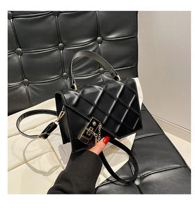 Detail of black quilted leather handbag with gold lock and chain on white textile