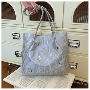 Dettaglio della borsa tote argento con farfalle metalliche e manico intrecciato su rivista