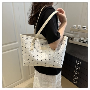 Dettaglio della borsa tote bianca con fiocchi neri e tracolla beige indossata