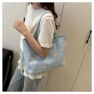 Detail of light blue tote bag featuring butterfly embroidery and embossed texture
