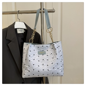 Détail du sac plissé tendance avec broderies de nœuds et bandoulière dorée
