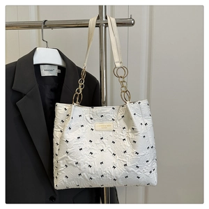 Détail du sac fourre-tout plissé blanc avec nœuds noirs et chaîne en métal doré