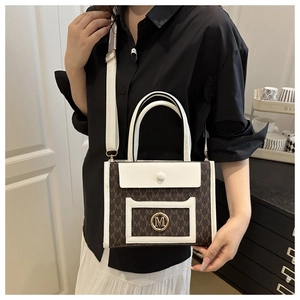 Detail view of large tote bag with brown monogram print, white handle, and gold M buckle