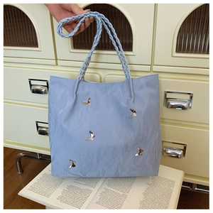 Dettaglio borsa tote azzurra con farfalle in metallo argentato e manici intrecciati
