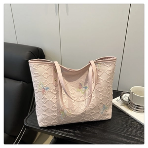 Détail d'un sac cabas rose clair en tissu texturé avec broderie de papillons colorés