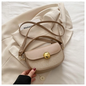 Detail of a chic half-round saddle bag featuring beige patchwork and golden ball clasp