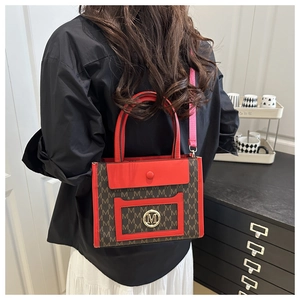 Detailed shot of a red and brown tote bag with M-pattern print and gold logo on a model