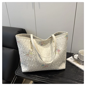 Détail d'un grand sac cabas blanc avec gaufrage en losange et broderies papillon colorées