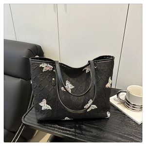 Détail de la broderie papillon colorée sur la surface texturée d'un sac cabas noir