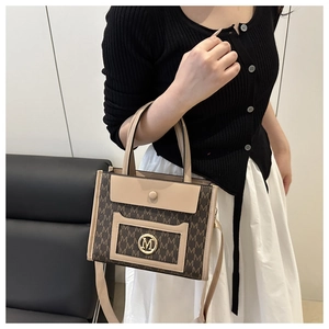 Detail of large tote bag with brown M-pattern print, gold logo, and beige trim accents