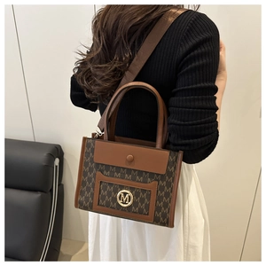 Detail of brown tote bag featuring all-over M pattern and golden circular logo