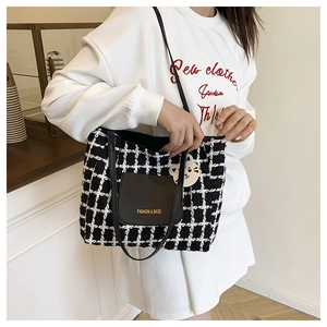Detail of checkered tote bag with leather pocket and cute cat charm in cafe setting