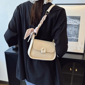Sac bandoulière crème avec chaîne foulard porté par un mannequin sur fond contrasté