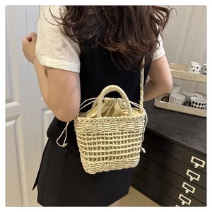 Detail of a beige woven straw bucket bag with drawstring liner and crossbody strap