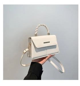 Détail d'un sac à main en cuir blanc avec poignée tressée et décoration en métal doré