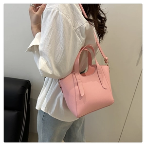 Pink lychee grain leather bucket bag shown on shoulder in a minimalist interior setting