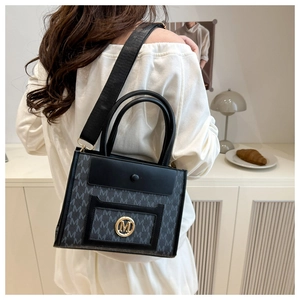 Detail of printed canvas tote bag with gold metal M logo and leather trim details