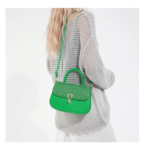 Sac à bandoulière vert avec rabat scintillant et boucle dorée porté par un modèle
