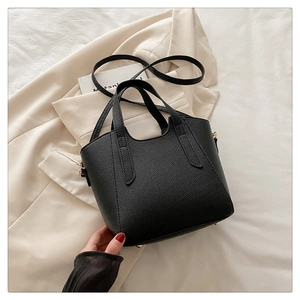 Detailed view of black litchi pattern leather handbag with golden metal bottom studs