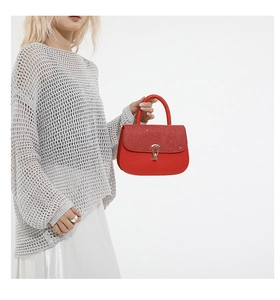 Détail d'un sac rouge avec rabat scintillant et fermoir tournant doré en goutte