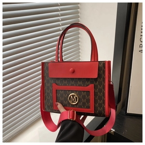 Close-up of the red leather front pocket with a round gold M metal logo on a tote bag