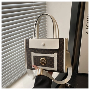 Detail of tote bag with brown M pattern, cream leather trim, and gold logo emblem
