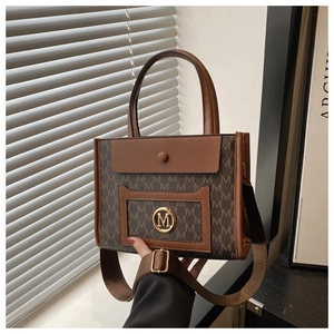 Detail of tote bag featuring brown monogram pattern and golden M logo with shoulder strap