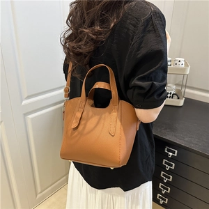 Brown litchi grain bucket bag with adjustable strap shown on model in home setting