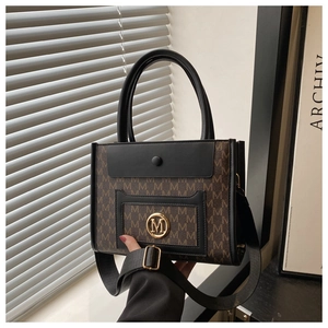 Detail of printed tote bag with golden M-logo and adjustable black shoulder strap