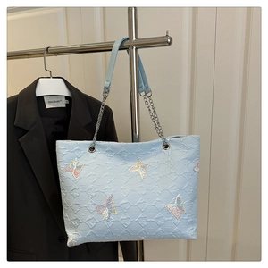 Close-up of light blue quilted tote bag with colorful butterfly embroidery and chain strap