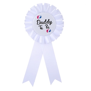 Detailed close-up of a white Daddy To Be badge with blue and red baby footprints