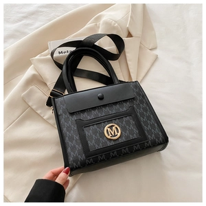 Close-up of black tote bag featuring gold M logo, monogram print, and wide fabric strap