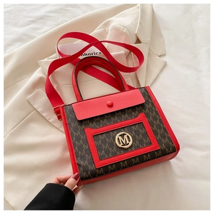 Detail of printed tote bag with golden metal M logo and wide red shoulder strap