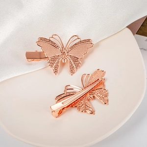 Detailed view of rose gold butterfly hair clips with intricate filigree on a ceramic tray