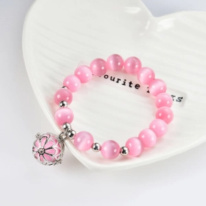 Close-up of pink cat eye beads bracelet with a hollow floral pendant on a white tray