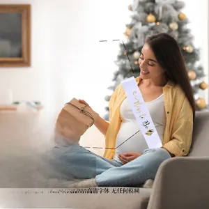 Detailed view of white satin Mom to Be sash with gold foil font in festive Christmas setting