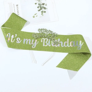 Close-up of green glitter sash and rhinestone birthday headband on a white surface